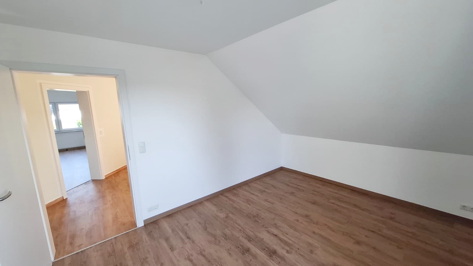 Helles Dachzimmer mit Holzboden und Durchgang zum Flur