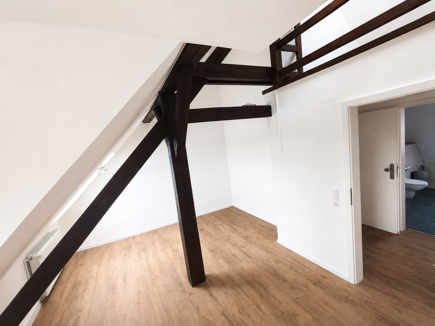 Dachraum mit hellen Wänden, dunklen Holzbalken und Brüstung